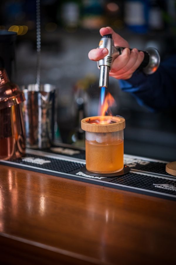 Bartender lighting a smoked cocktail under a wooden lid