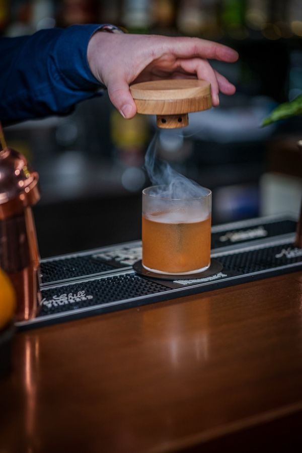 Smoke curling out of a cocktail as the lid comes off