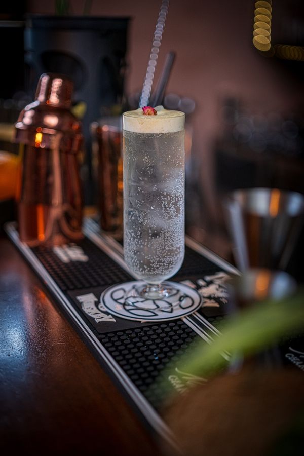 Tall fizzy cocktail with a flower garnish beside a copper shaker