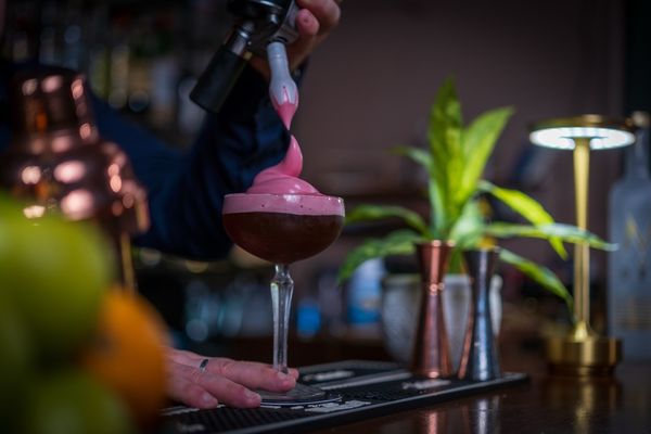 Bartender topping a coupe cocktail with pink foam