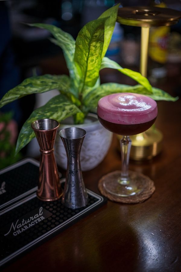 Deep red cocktail with a foam top beside copper jiggers